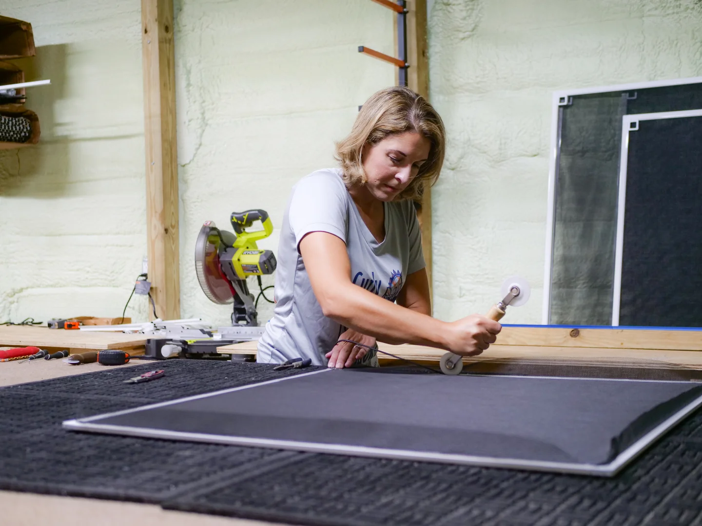Kristen carefully rolling screen material into a frame at the workbench
